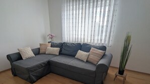 Um sofá modular cinzento com almofadas estampadas, um tapete felpudo branco e um vaso de planta.