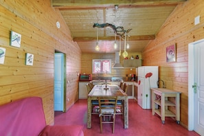 A cozy cabin interior with a wooden dining table, chairs, a red couch, a kitchen area with appliances, and a unique ceiling light fixture.