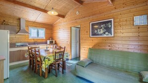 En hyggelig hytte med træpaneler, et spiseområde med bord og stole, en grøn sofa og et køkken med komfur og vask.