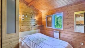 A wooden-paneled room with a bed, a window with a view of greenery, and a small kitchenette area. - Gite des fleurs - Pervenche (Saint-Prix)