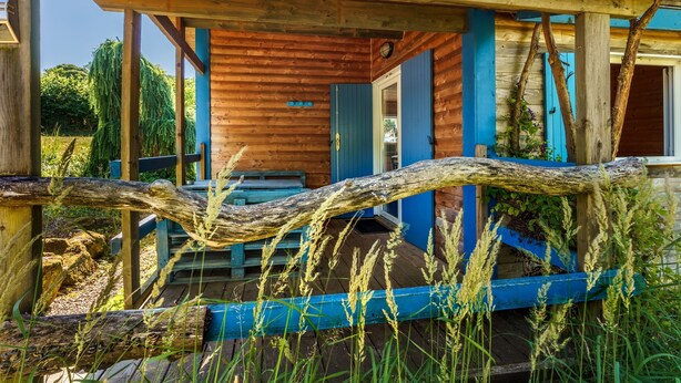 A rustic wooden cabin with a porch, a blue door, and a wooden deck. - Gite des fleurs - Pervenche (Saint-Prix)