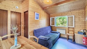A wooden cabin with a sofa, a dining table, and a vase with dried plants. - Gite des fleurs - Pervenche (Saint-Prix)