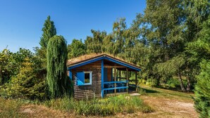 A rustic cabin with a thatched roof, surrounded by dense greenery and tall trees. - Gite des fleurs - Pervenche (Saint-Prix)