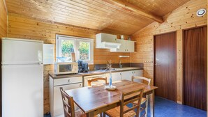 A compact kitchen with wooden walls, a dining table, and a refrigerator. - Gite des fleurs - Pervenche (Saint-Prix)