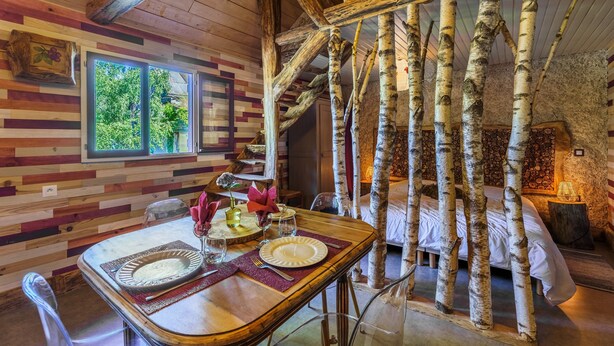 A rustic room with birch tree decor, a dining table set with plates and glasses, and a bed with white bedding.
