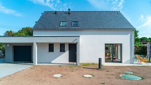 Ein modernes, zweistöckiges Haus mit flachem Dach, einer Garage und einer überdachten Terrasse.