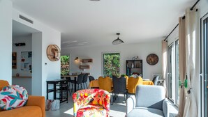 Ein modernes Wohnzimmer mit einem farbenfrohen Sessel, einem grauen Sofa und einem Essbereich mit gelben Stühlen.