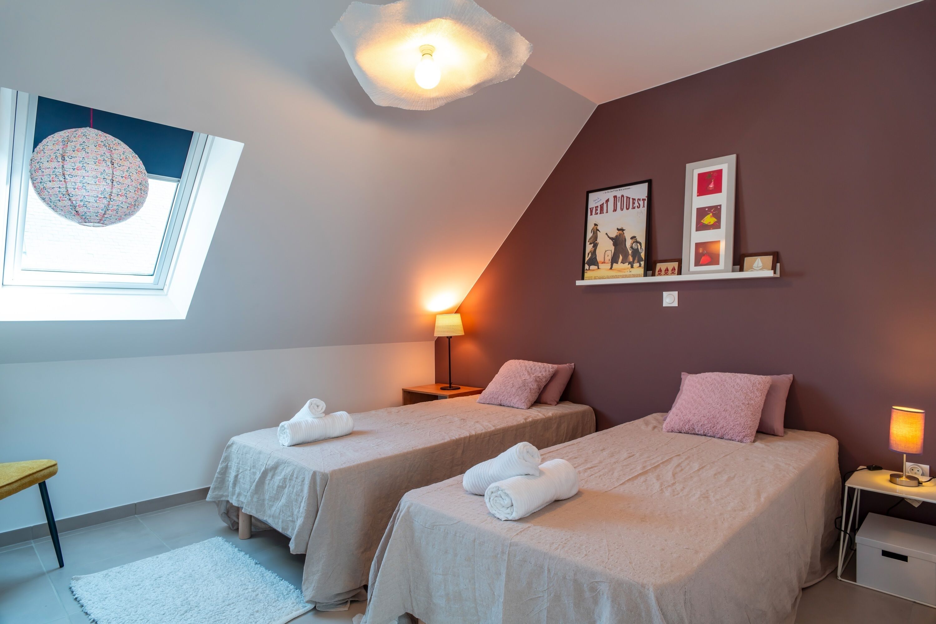 Une chambre avec deux lits, un puits de lumière, un globe décoratif et un mur orné de tableaux encadrés.