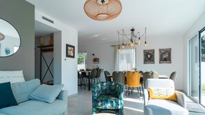 A modern living room with a sofa, armchair, and coffee table. There is a dining area with chairs and a table in the background. - Maison HG - Presqu'ile de Crozon (Plomodiern)
