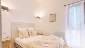 Un dormitorio ordenado con cama, mesitas de noche y una ventana con cortinas ligeras.