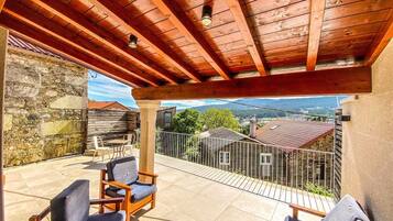 Une terrasse couverte avec des poutres en bois, un mur en pierre et une vue sur les maisons au loin.