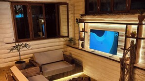 A cozy cabin interior with a wooden sofa, a TV mounted on a wall, and a small table with plants. - Solar Kaeté (Santo Amaro do Maranhão)