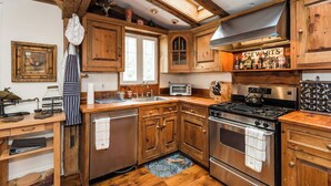 Una cocina rústica con armarios de madera, una estufa a gas, un horno empotrado y una ventana sobre el fregadero.