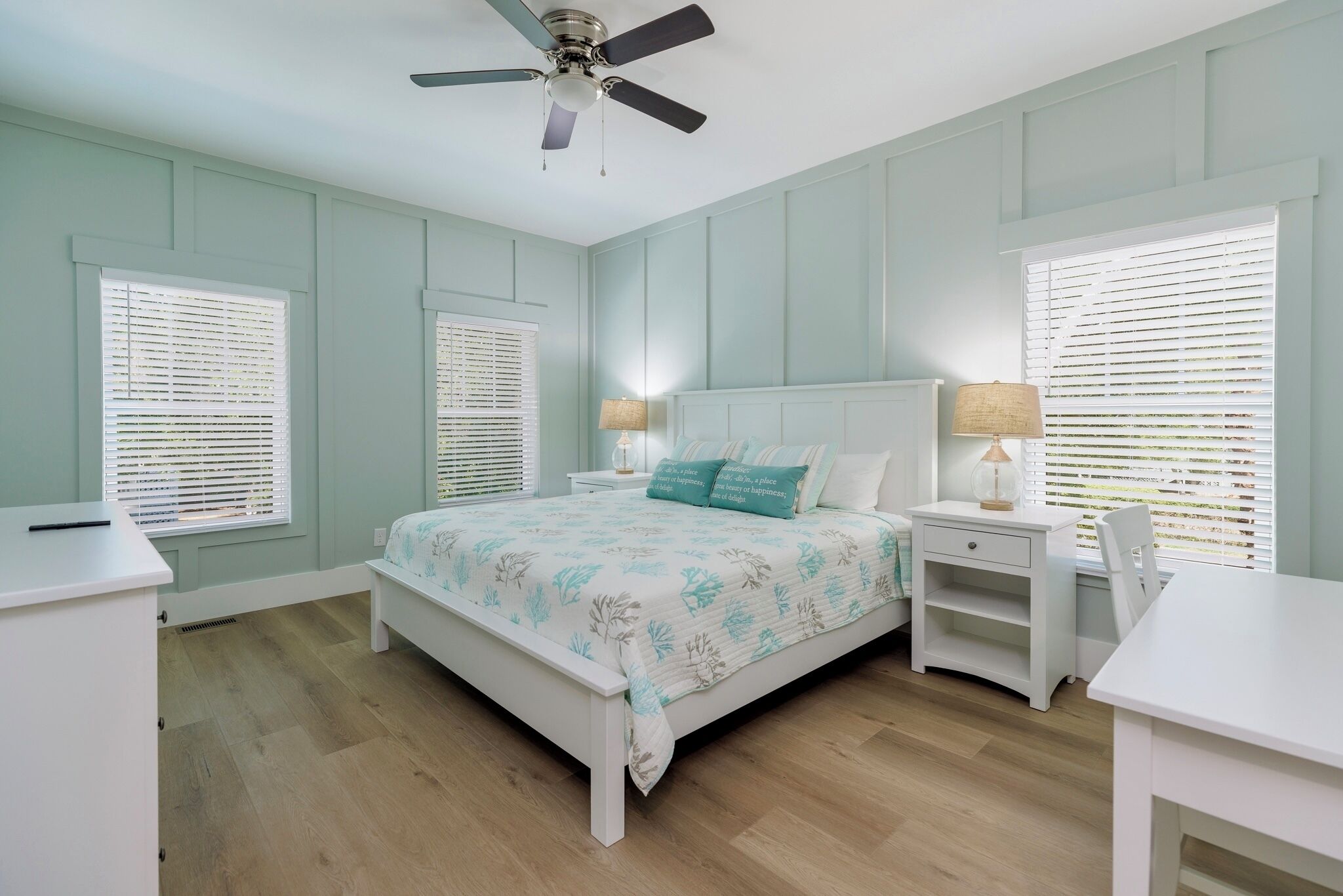 A bedroom with a bed, nightstands, a desk, and a ceiling fan.