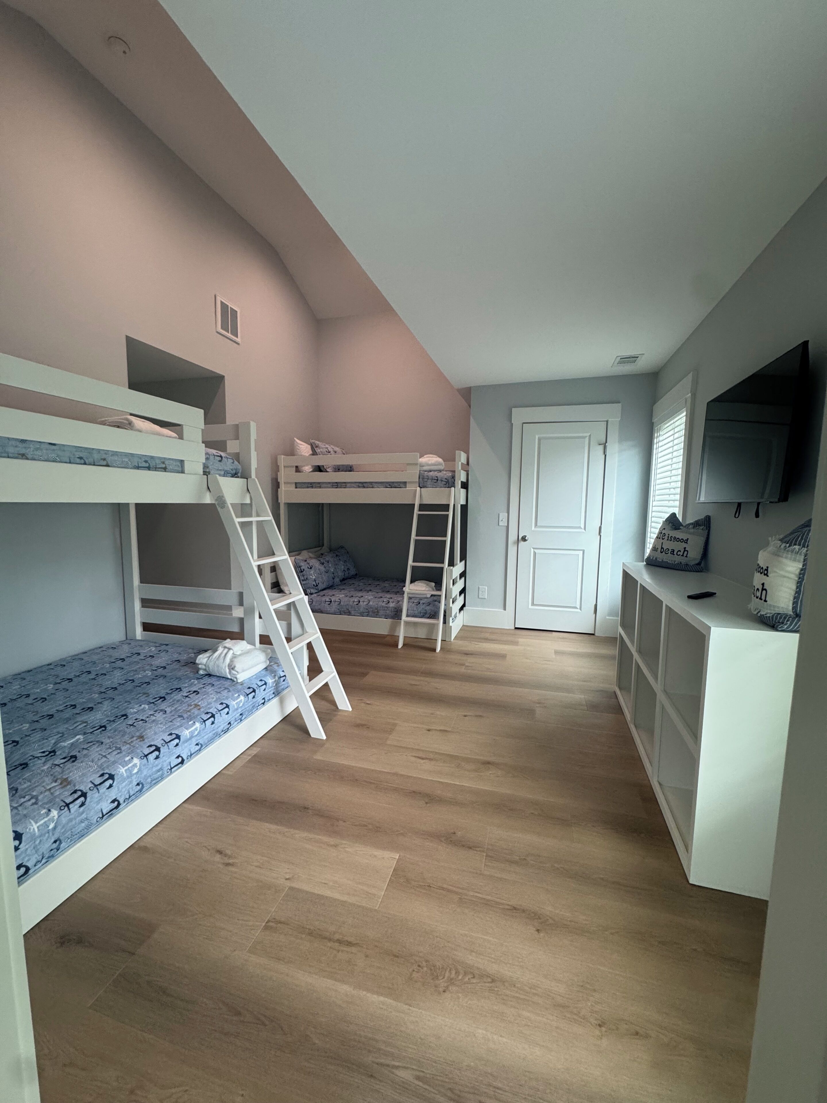 A room with bunk beds, a ladder, a door, and a television on a cabinet.