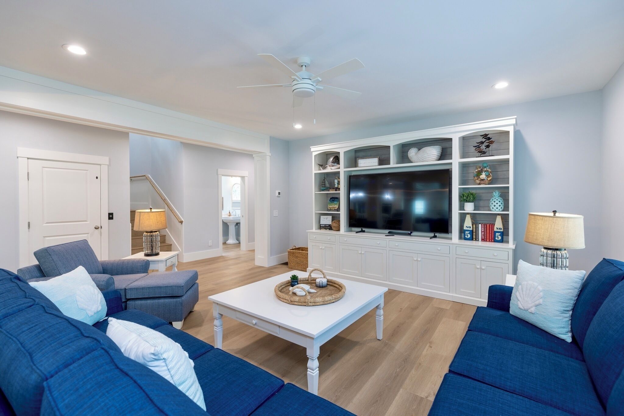 Una sala moderna con un mueble blanco para entretenimiento, sofás azules y un ventilador de techo.