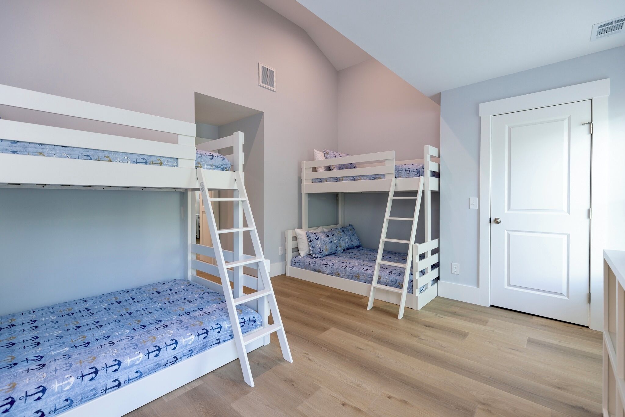 Een kamer met stapelbedden, een deur en een witte muur.