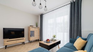 A modern living room with a flat-screen TV, a sofa, a coffee table with fruit, and a wooden cabinet.