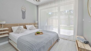 A modern bedroom with a large bed, bedside tables, a bedside lamp, a decorative wall hanging, and a view through a large window. - Elegant Apartment | 150 m from the Beach, Terrace, Parking (Międzywodzie)