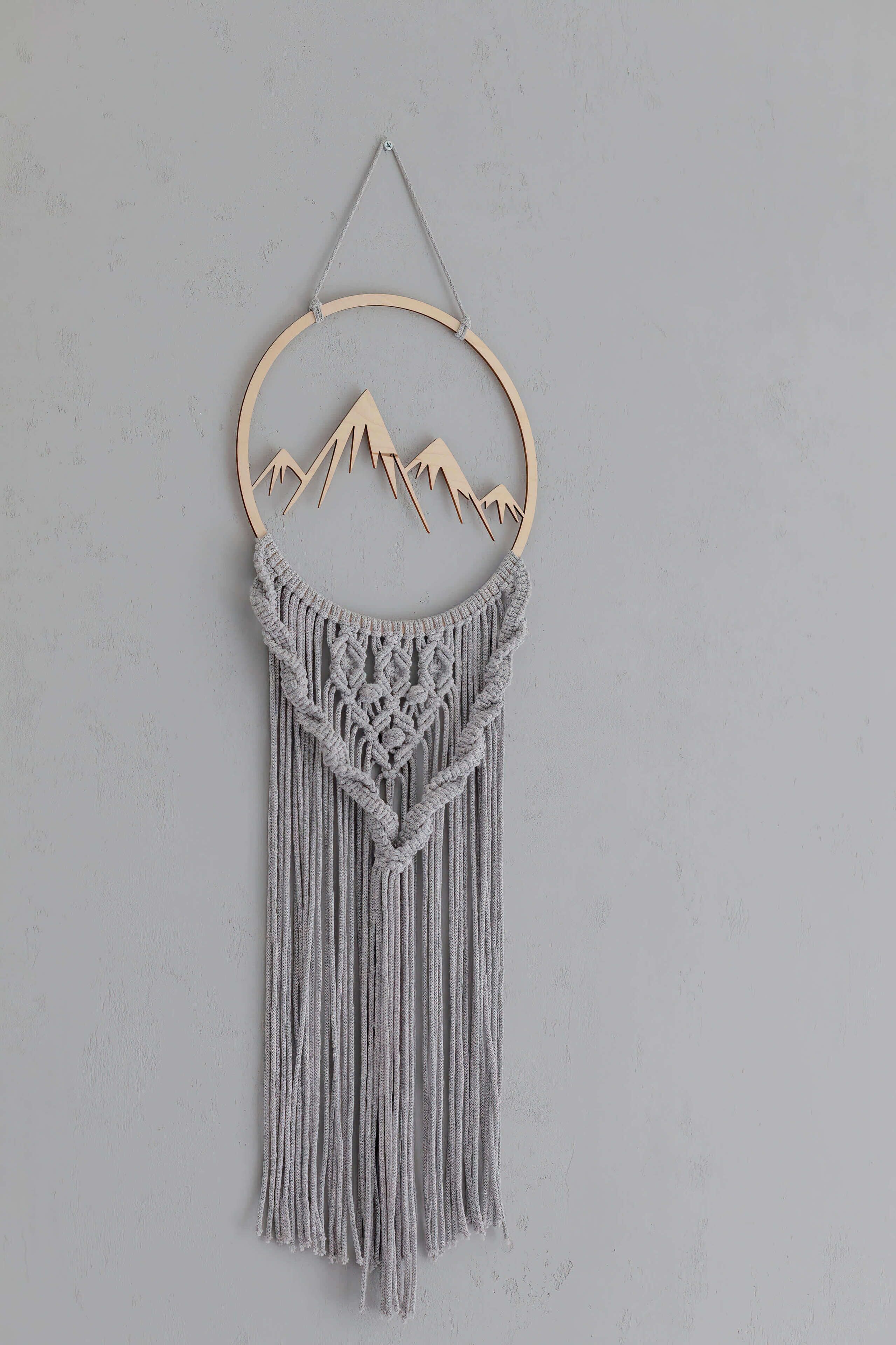 Une décoration murale en macramé représentant une montagne et un arbre.