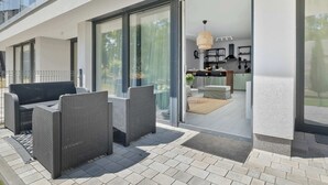 A modern outdoor patio with wicker furniture and a glass door leading to a kitchen area. - Elegant Apartment | 150 m from the Beach, Terrace, Parking (Międzywodzie)
