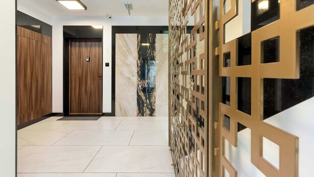 Un pasillo moderno con puerta de madera, pared de mármol y separador metálico decorativo.