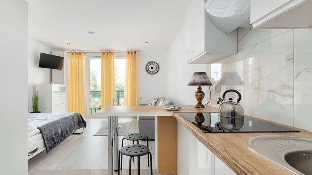 Una cocina moderna con encimera de madera, un lavamanos, una tetera y un comedor con mesa y sillas.