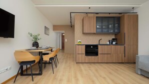 A modern kitchen with wooden cabinets, a built-in oven, and a coffee machine. There is a dining area with a table and chairs. - Cozy Apartment in the Heart of the Old Town | Smart TV and Wi-Fi (Warszawa)
