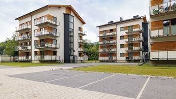 A modern apartment building with multiple balconies, a paved courtyard, and a grassy area.