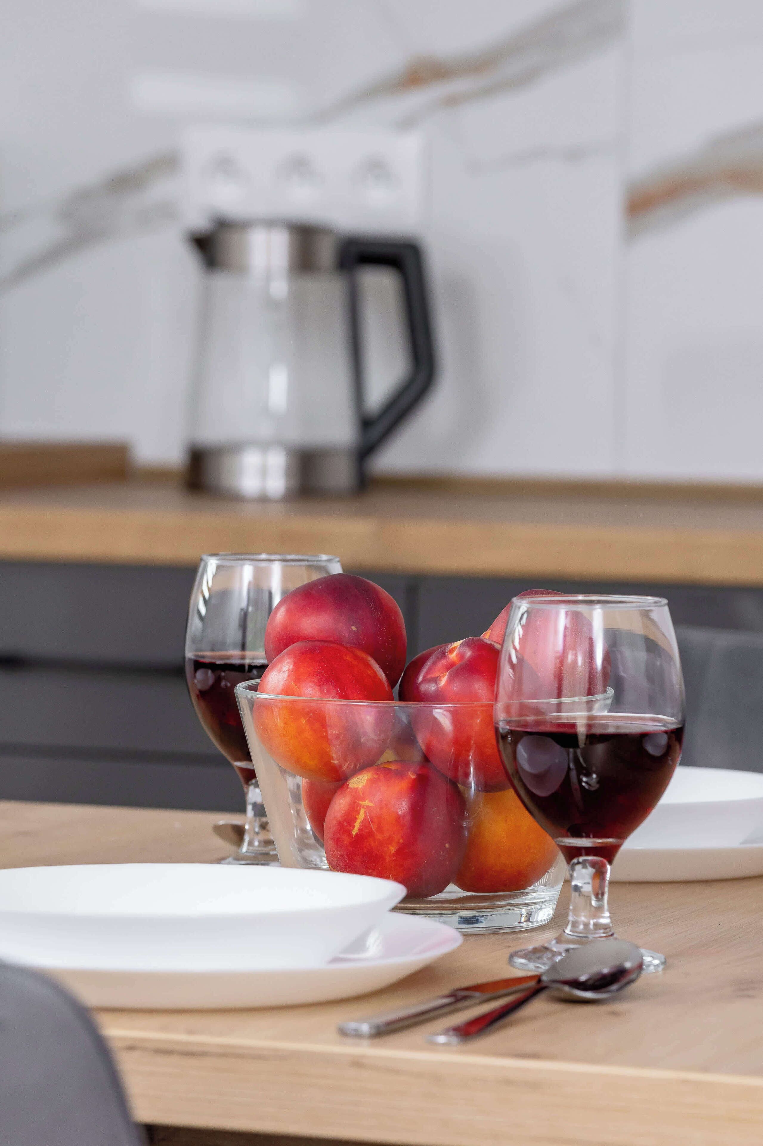 A kitchen counter with a fruit bowl containing peaches and a glass of red wine.