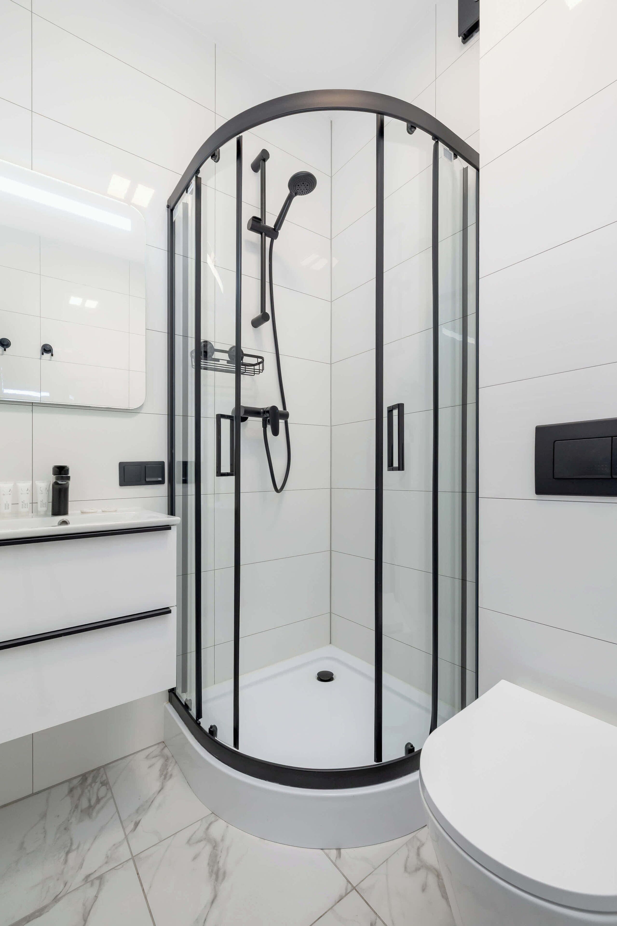 Une salle de bain moderne avec une douche à parois de verre, des toilettes blanches et un meuble-lavabo avec un miroir.
