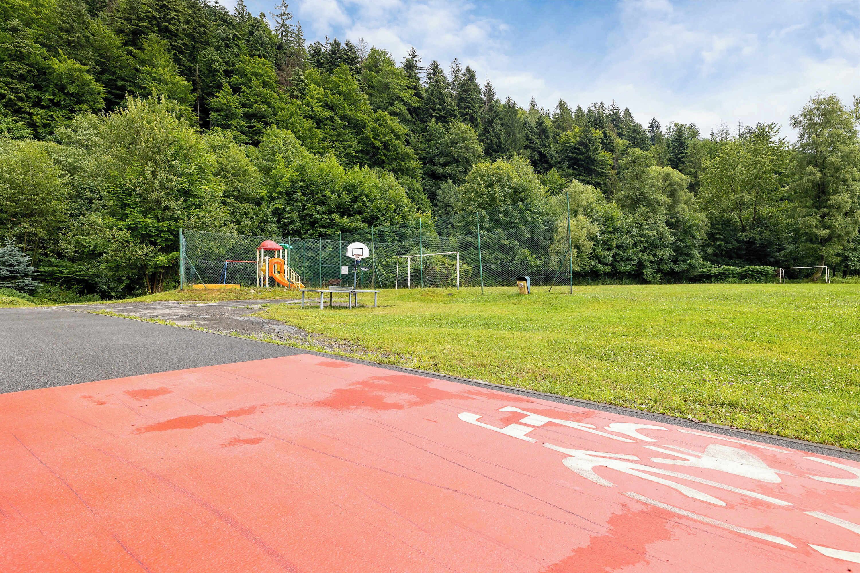 A red bike lane with a basketball court and a soccer goal in a park.