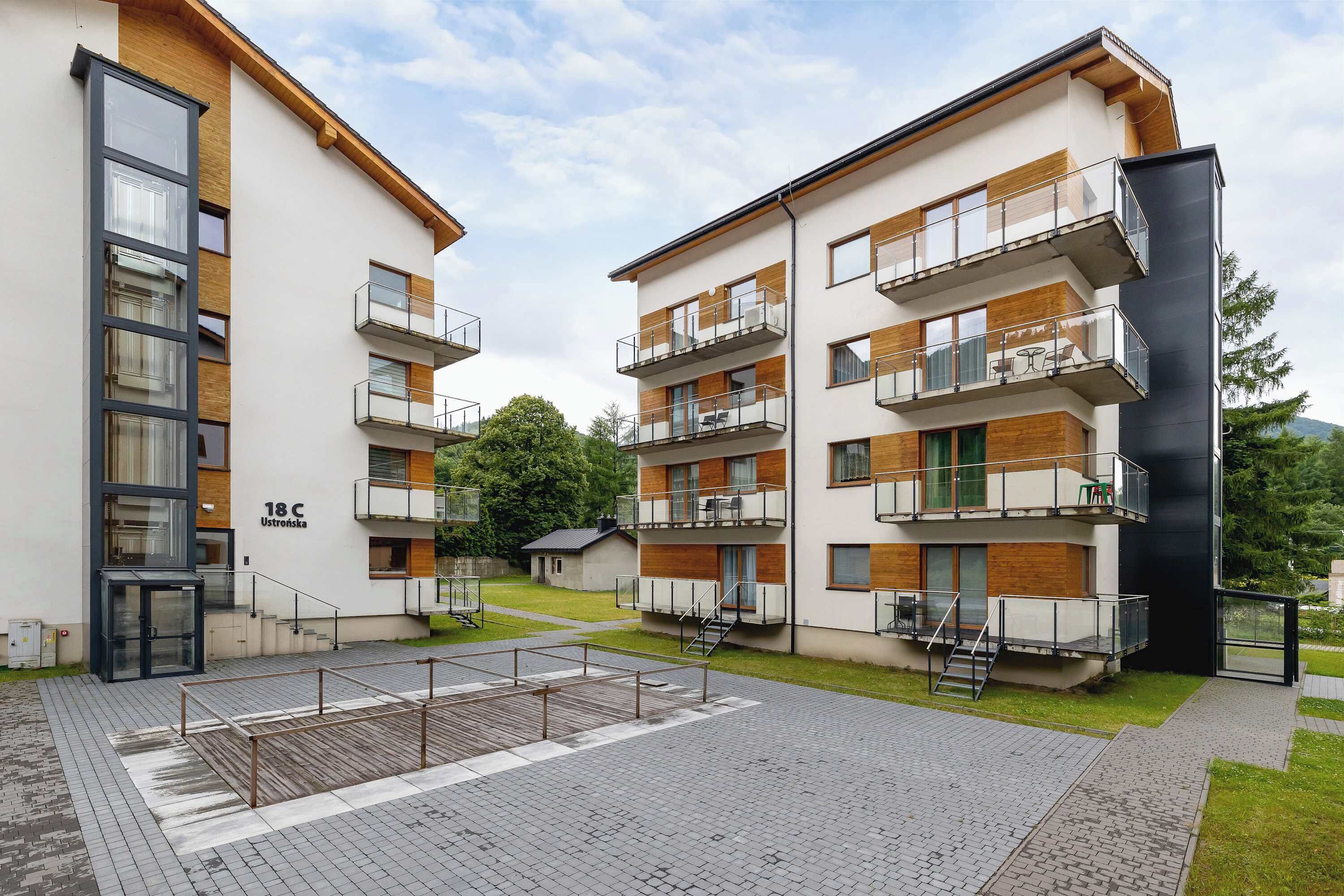 Un immeuble d’appartements moderne doté de nombreux balcons, d’une entrée abritée et d’un petit espace extérieur aménagé pour s’asseoir.