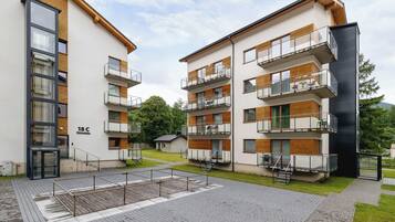 Un immeuble d’appartements moderne doté de nombreux balcons, d’une entrée abritée et d’un petit espace extérieur aménagé pour s’asseoir.