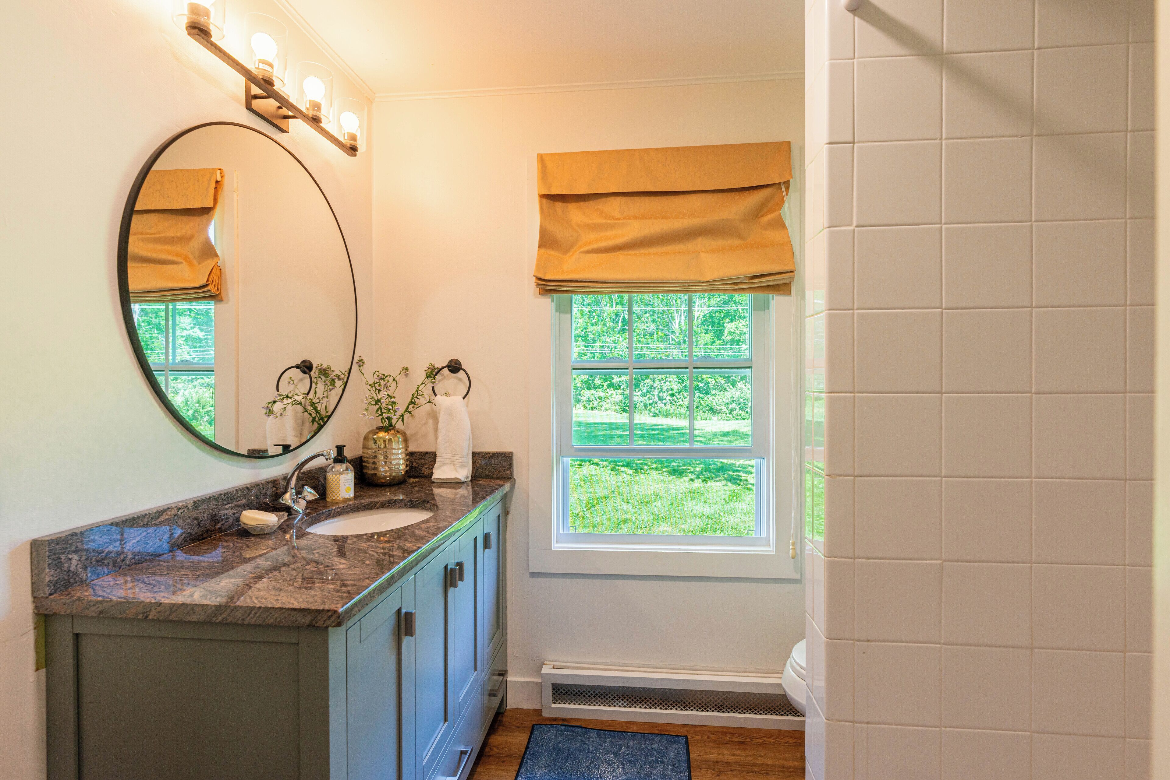 A bathroom with a marble sink, a large mirror, and a window with a view of greenery.