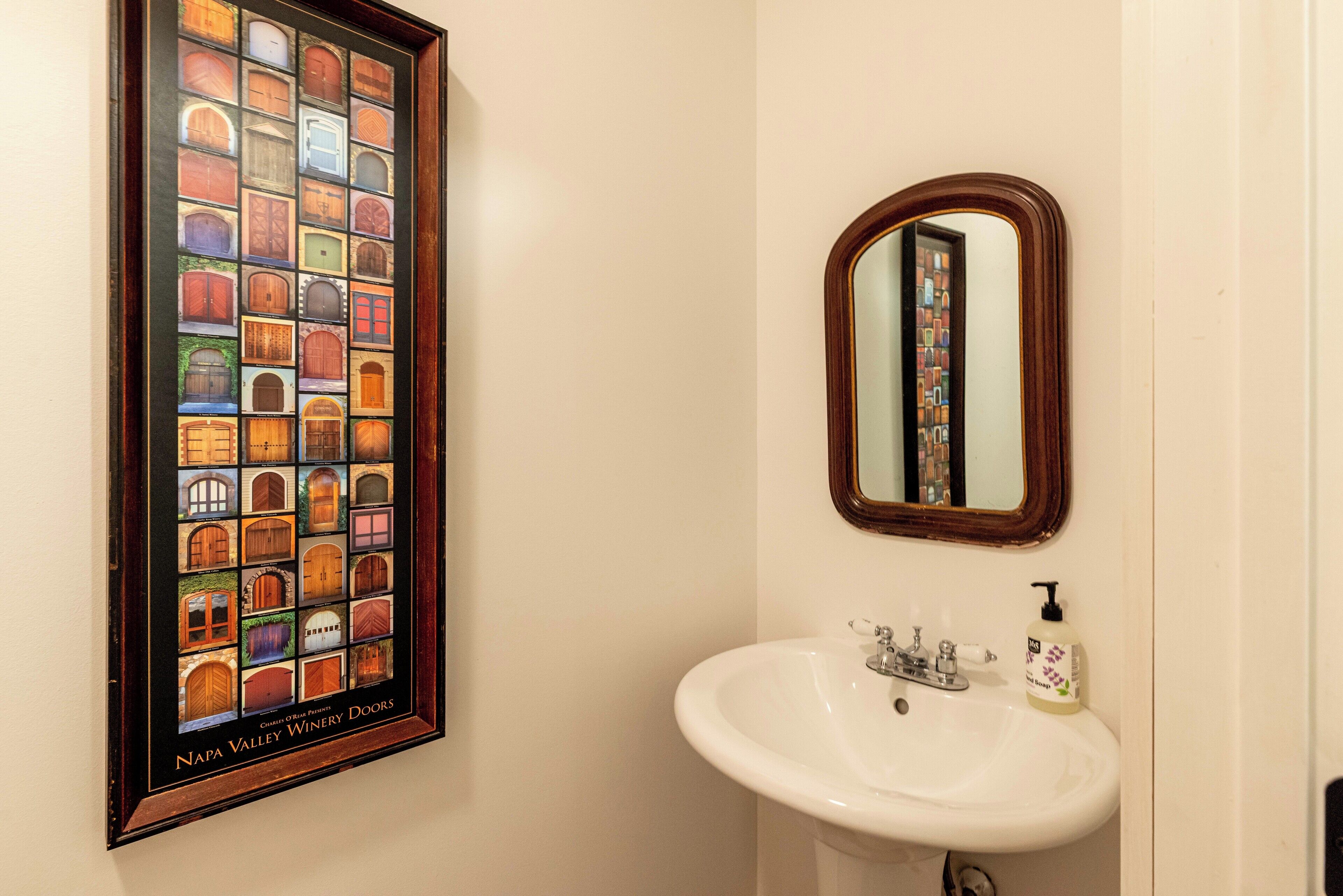 A bathroom with a framed picture of Napa Valley winery doors, a white sink, and a mirror.