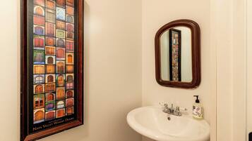 A bathroom with a framed picture of Napa Valley winery doors, a white sink, and a mirror.