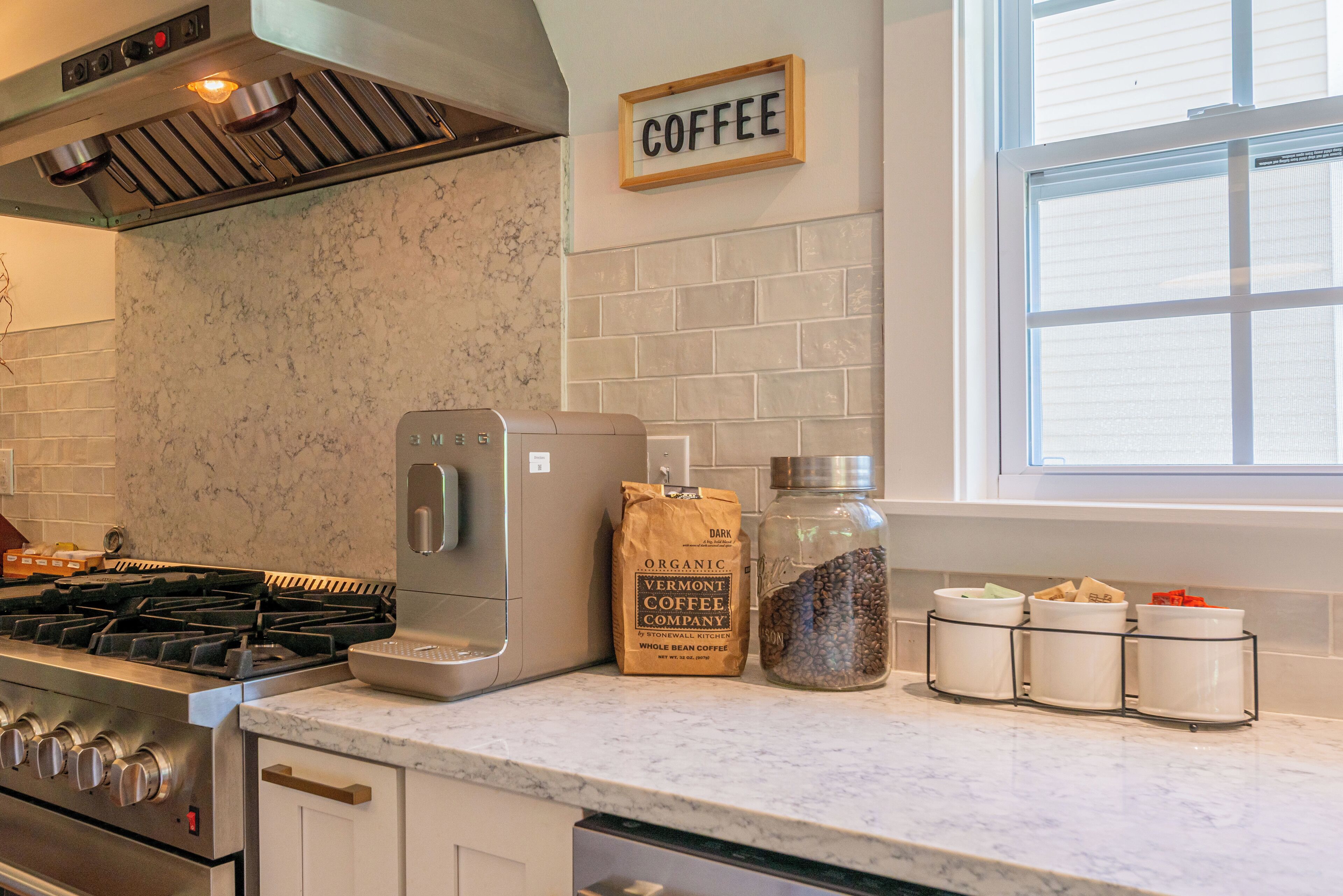 Una cocina con cafetera, un paquete de café en grano y tarros de granos de café.