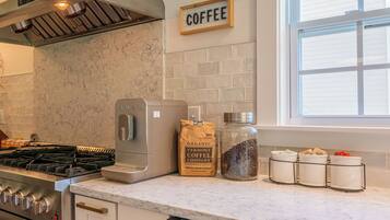 Una cocina con cafetera, un paquete de café en grano y tarros de granos de café.