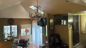 A spacious living room with a chandelier, a sofa, a coffee table, and a chair. There is a large window with curtains, a television, and a framed map on the wall.