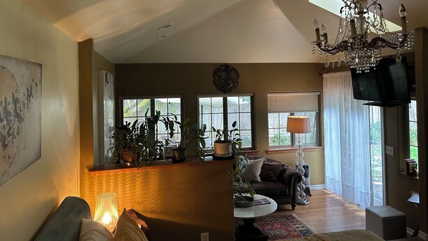 A spacious living room with a high ceiling, a chandelier, a television, and a large window with curtains.