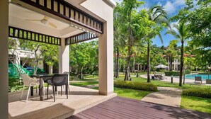 A covered outdoor area with a table and chairs, a pool, and surrounding greenery. - Laguna Village, Two-Bedroom 138/25 Townhouse (Cherngtalay)