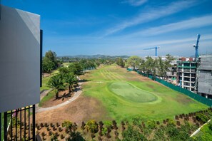 Un campo de golf con cielo despejado, palmeras y grúas de construcción al fondo.