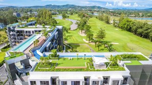 Un hotel moderno con piscina en la azotea, campo de golf y abundante vegetación.