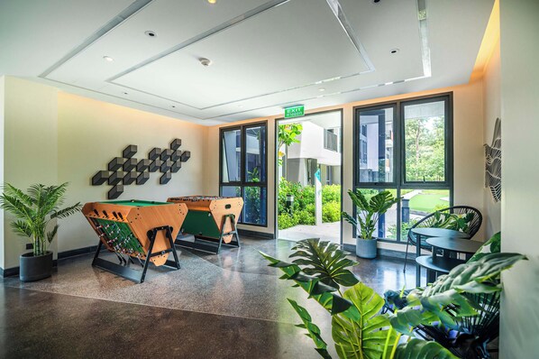 Un moderno vestíbulo con una mesa de fútbol, plantas en macetas y vistas al exterior.