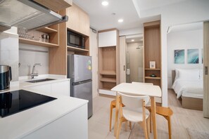 Una cocina moderna con microondas integrado, refrigerador y cocina por inducción negra. Hay una mesa de comedor blanca con dos sillas.