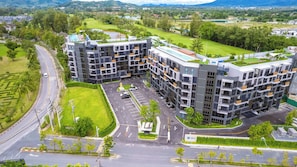 A modern apartment complex with multiple buildings, a parking area, and a golf course in the background.