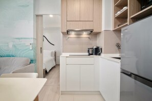 Una kitchenette compacta con un refrigerador de acero inoxidable, una cafetera y armarios de madera.