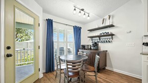 A dining area with a round table, chairs, and a kitchen with shelves above. - Salty Tradewind Retreat – Just One Mile to the Beach (St. Augustine)