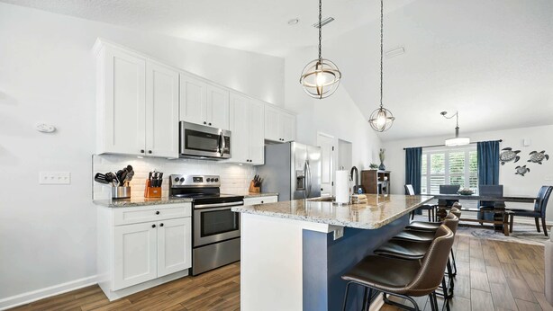 A modern kitchen with white cabinets, stainless steel appliances, a central island with bar stools, and a dining area with a view. - Salty Tradewind Retreat – Just One Mile to the Beach (St. Augustine)